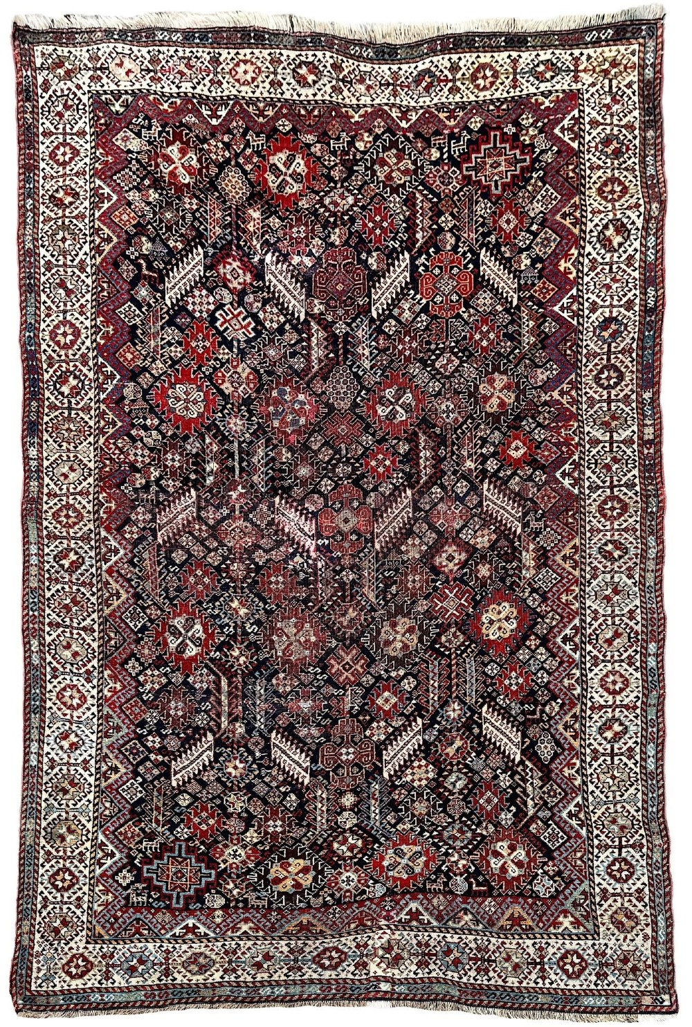 An antique Shekarlu tribal wool rug featuring dense dark navy and red geometric motifs enclosed by a patterned ivory border.