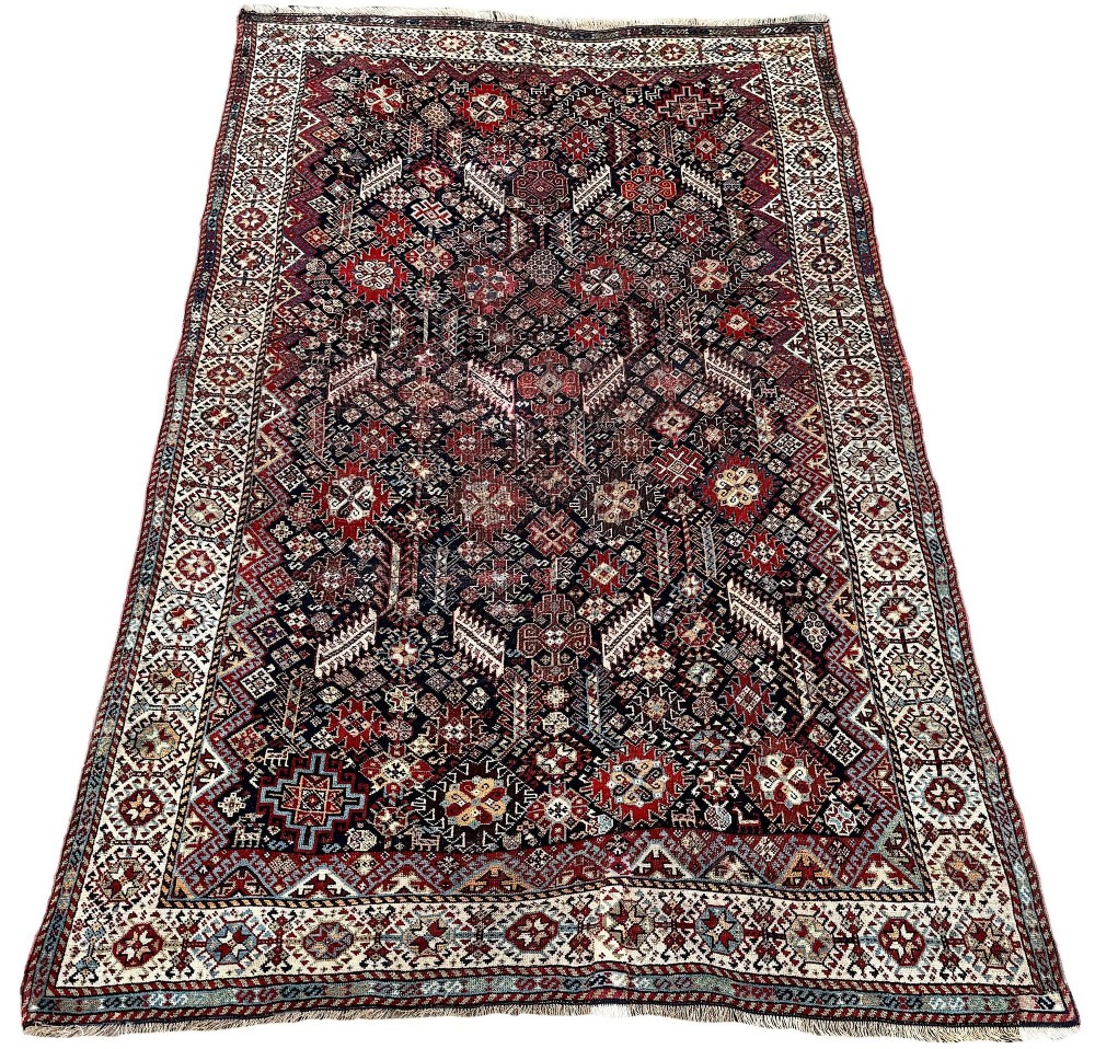 An antique Shekarlu tribal wool rug featuring dense dark navy and red geometric motifs enclosed by a patterned ivory border. View II