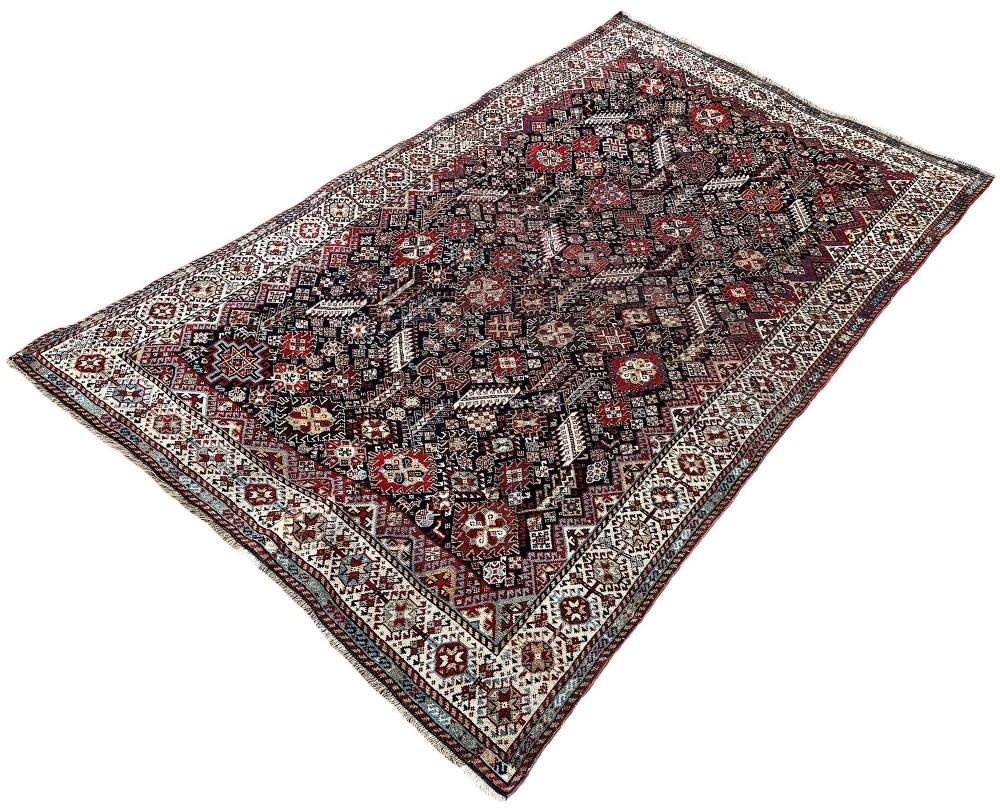 An antique Shekarlu tribal wool rug featuring dense dark navy and red geometric motifs enclosed by a patterned ivory border. View III