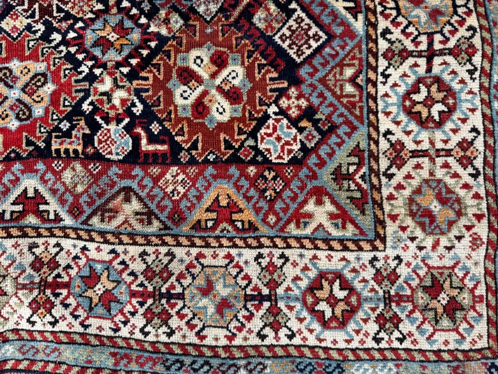 An antique Shekarlu tribal wool rug featuring dense dark navy and red geometric motifs enclosed by a patterned ivory border. View VI