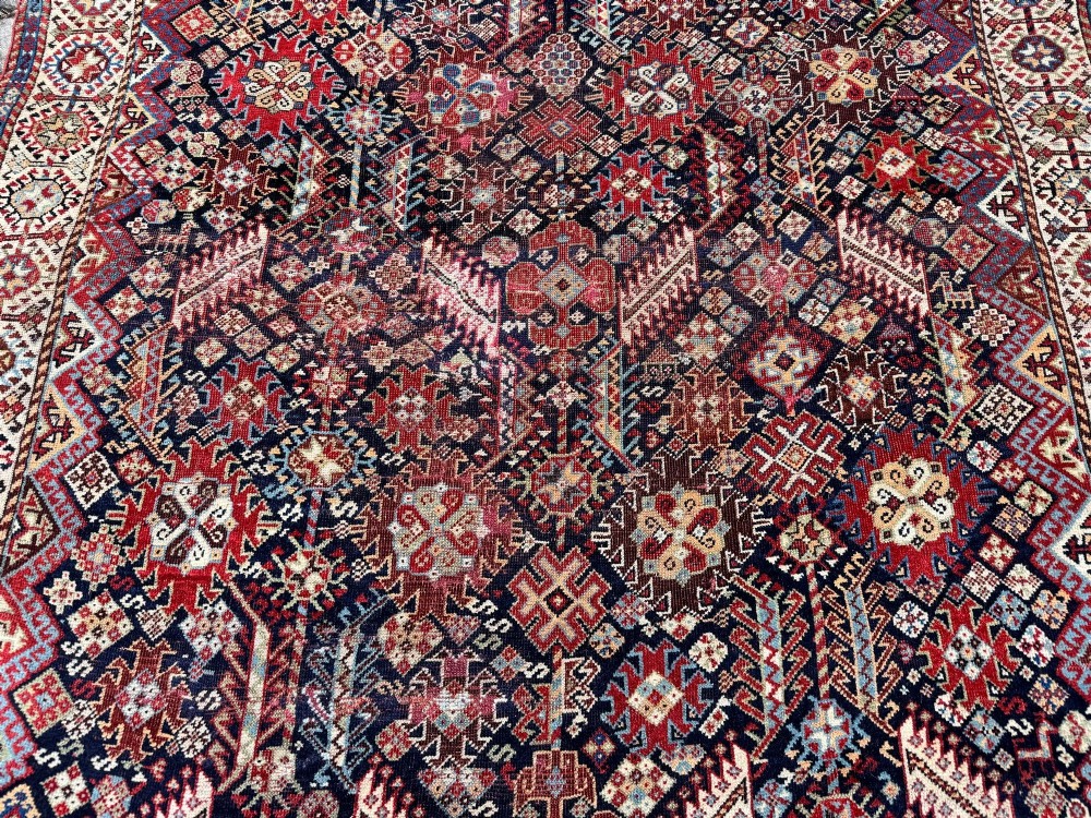 An antique Shekarlu tribal wool rug featuring dense dark navy and red geometric motifs enclosed by a patterned ivory border. View VII