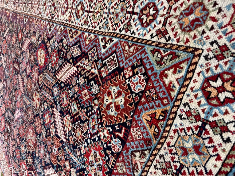 An antique Shekarlu tribal wool rug featuring dense dark navy and red geometric motifs enclosed by a patterned ivory border. View VIII