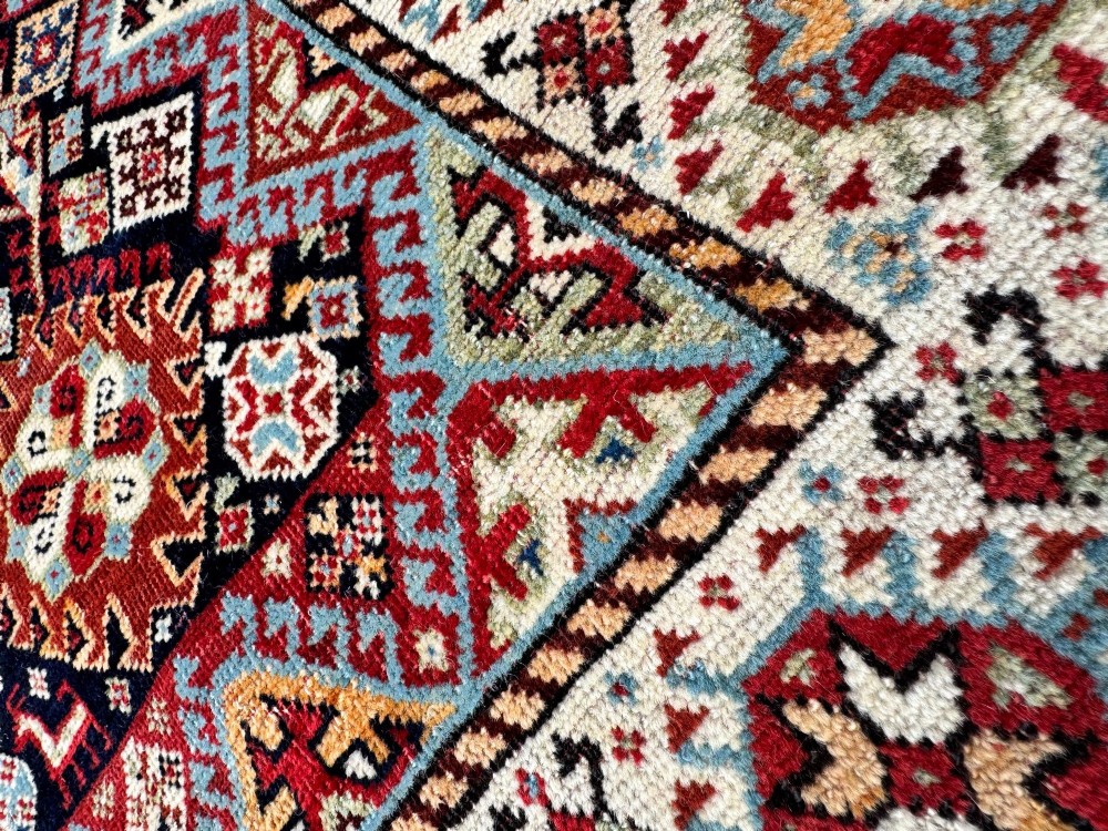 An antique Shekarlu tribal wool rug featuring dense dark navy and red geometric motifs enclosed by a patterned ivory border. View IX