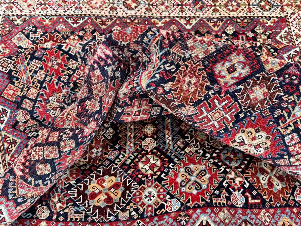 An antique Shekarlu tribal wool rug featuring dense dark navy and red geometric motifs enclosed by a patterned ivory border. View XI