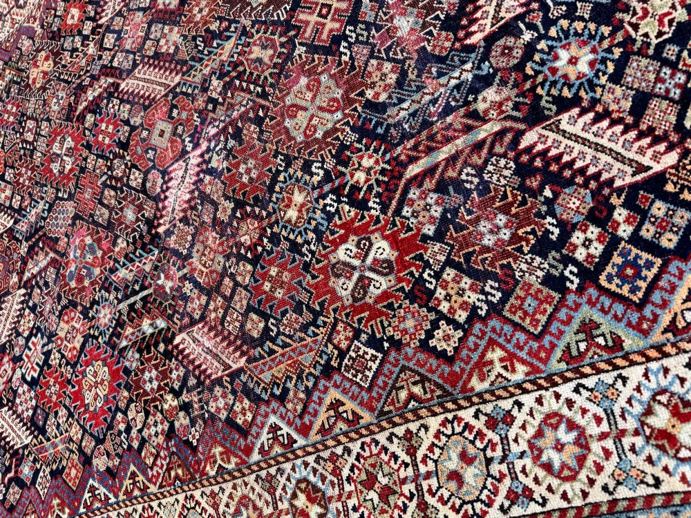 An antique Shekarlu tribal wool rug featuring dense dark navy and red geometric motifs enclosed by a patterned ivory border. View XII
