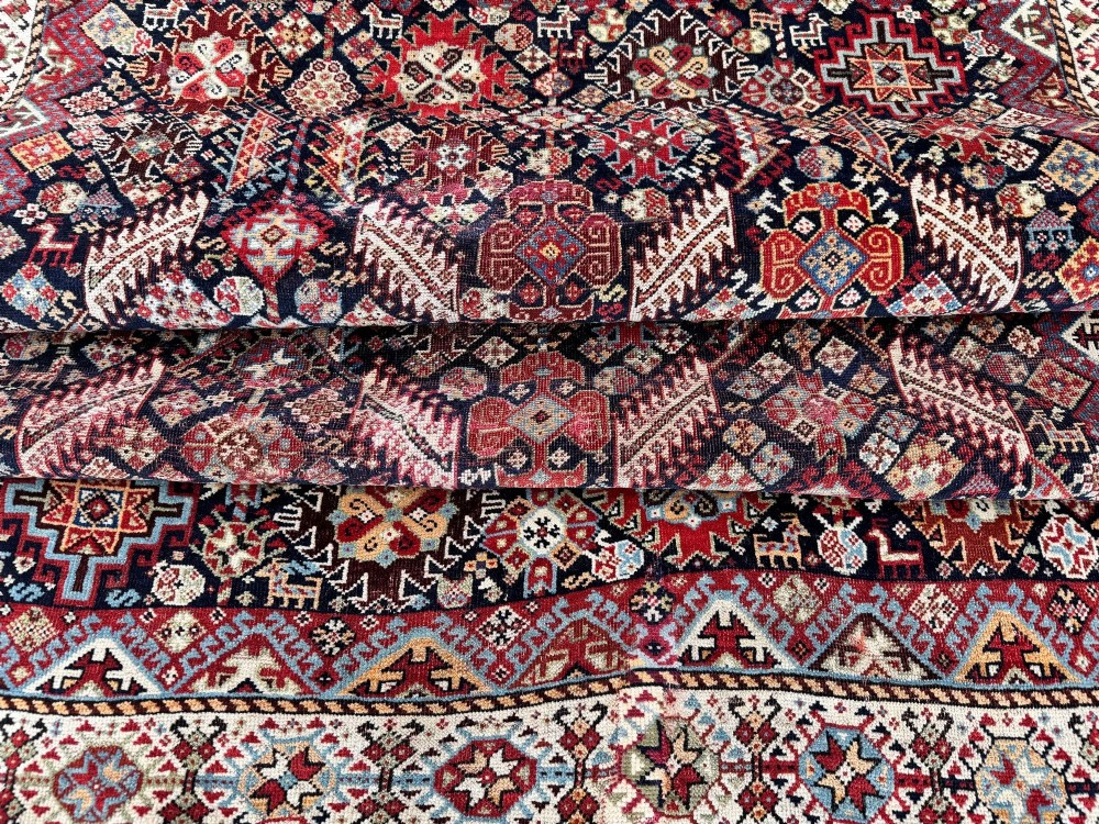 An antique Shekarlu tribal wool rug featuring dense dark navy and red geometric motifs enclosed by a patterned ivory border. View XIII