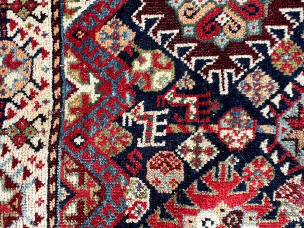 An antique Shekarlu tribal wool rug featuring dense dark navy and red geometric motifs enclosed by a patterned ivory border. View XIV