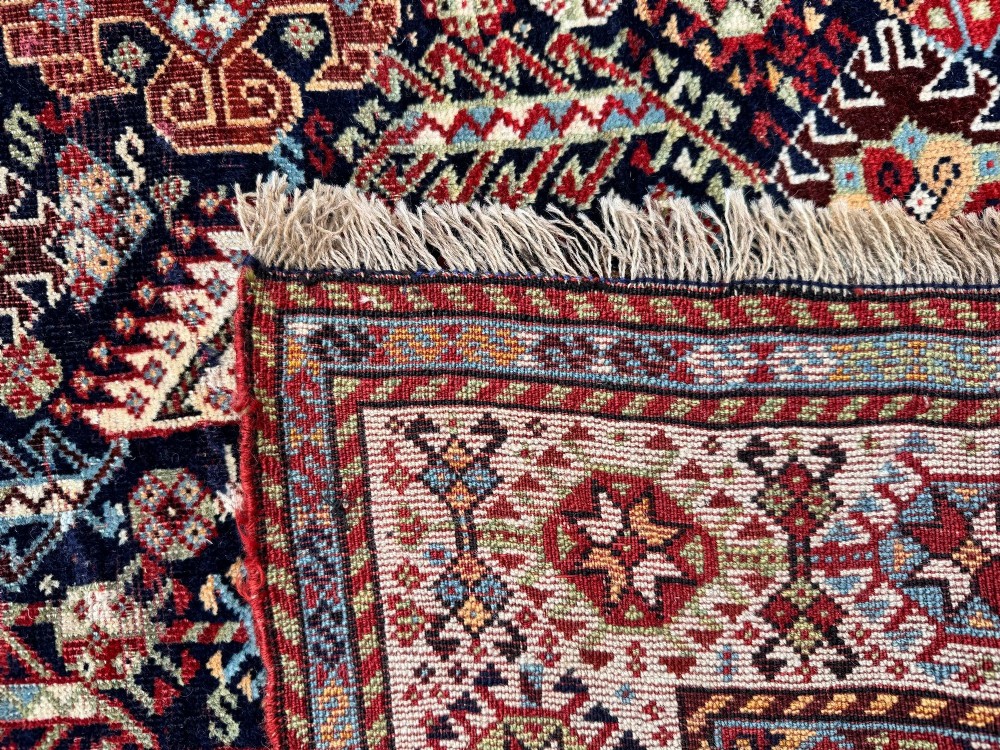 An antique Shekarlu tribal wool rug featuring dense dark navy and red geometric motifs enclosed by a patterned ivory border. View XV