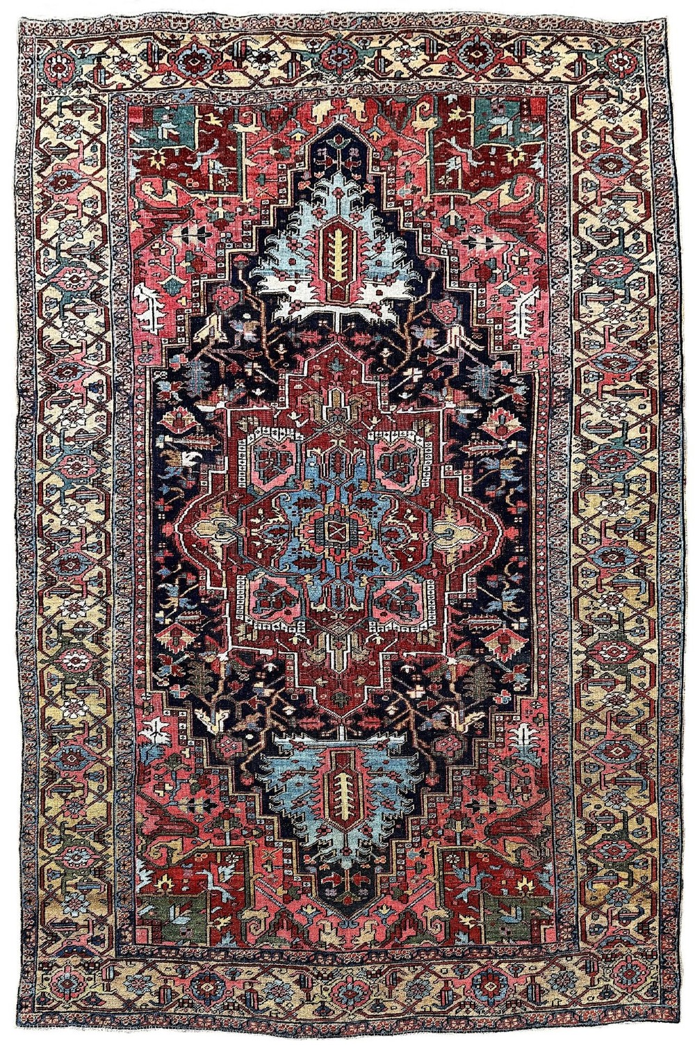 An antique Persian Heriz wool carpet featuring a large central geometric medallion in navy blue and light blue, set against a terracotta red field with broad angular floral borders.