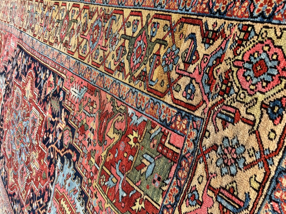 An antique Persian Heriz wool carpet featuring a large central geometric medallion in navy blue and light blue, set against a terracotta red field with broad angular floral borders. View IX