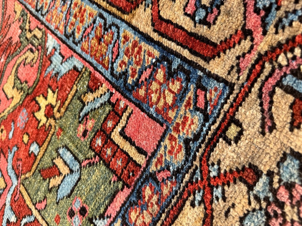 An antique Persian Heriz wool carpet featuring a large central geometric medallion in navy blue and light blue, set against a terracotta red field with broad angular floral borders. View X