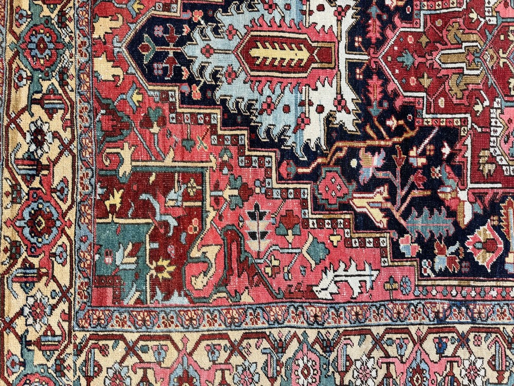 An antique Persian Heriz wool carpet featuring a large central geometric medallion in navy blue and light blue, set against a terracotta red field with broad angular floral borders. View XII