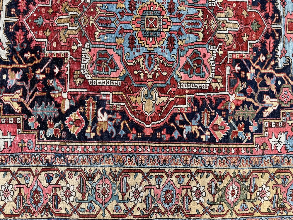 An antique Persian Heriz wool carpet featuring a large central geometric medallion in navy blue and light blue, set against a terracotta red field with broad angular floral borders. View XIII
