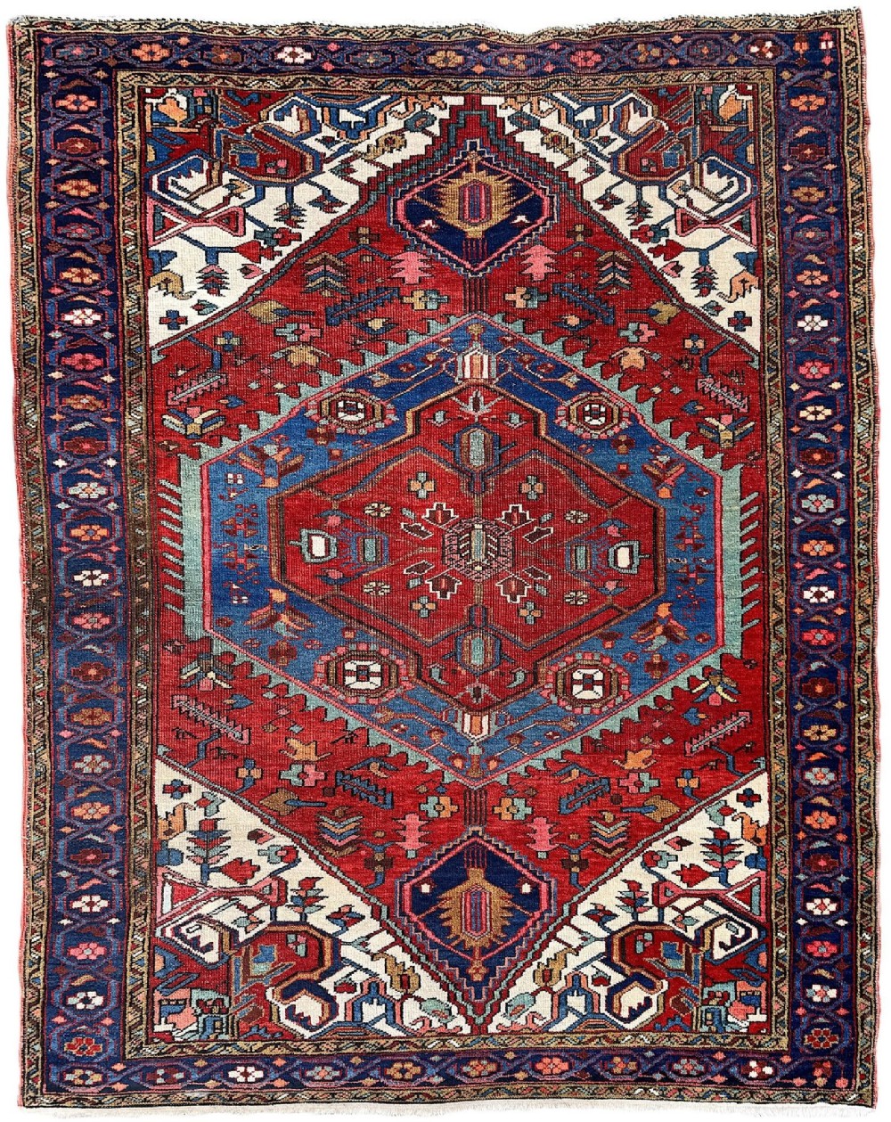 An antique Heriz wool rug featuring a large geometric central medallion in blue and red surrounded by cream spandrels and a navy border.