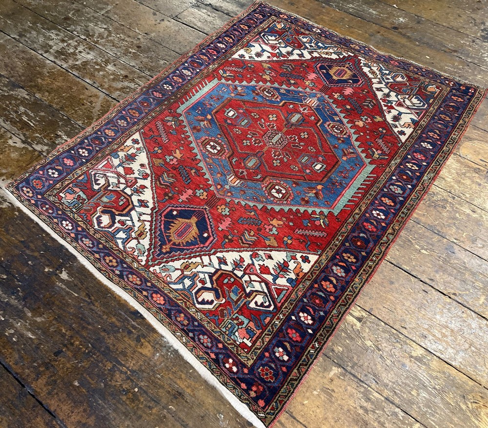 An antique Heriz wool rug featuring a large geometric central medallion in blue and red surrounded by cream spandrels and a navy border. View V