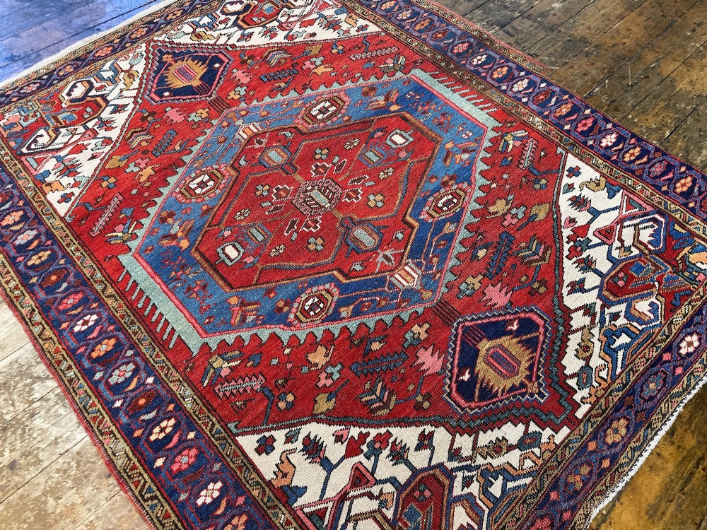 An antique Heriz wool rug featuring a large geometric central medallion in blue and red surrounded by cream spandrels and a navy border. View VI