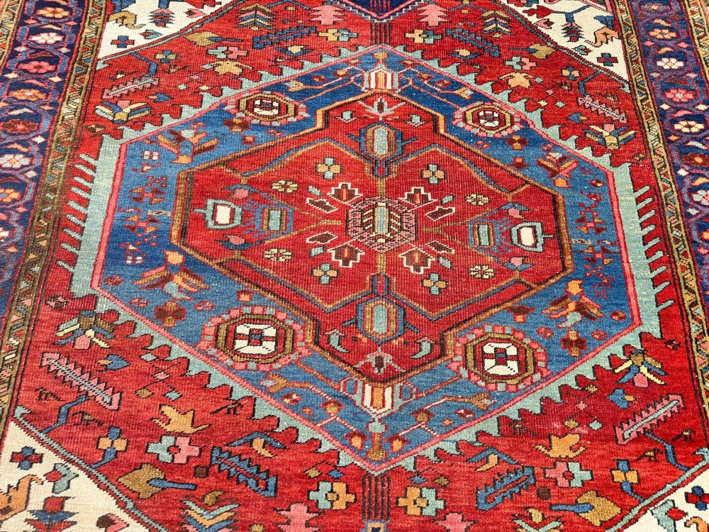 An antique Heriz wool rug featuring a large geometric central medallion in blue and red surrounded by cream spandrels and a navy border. View VIII
