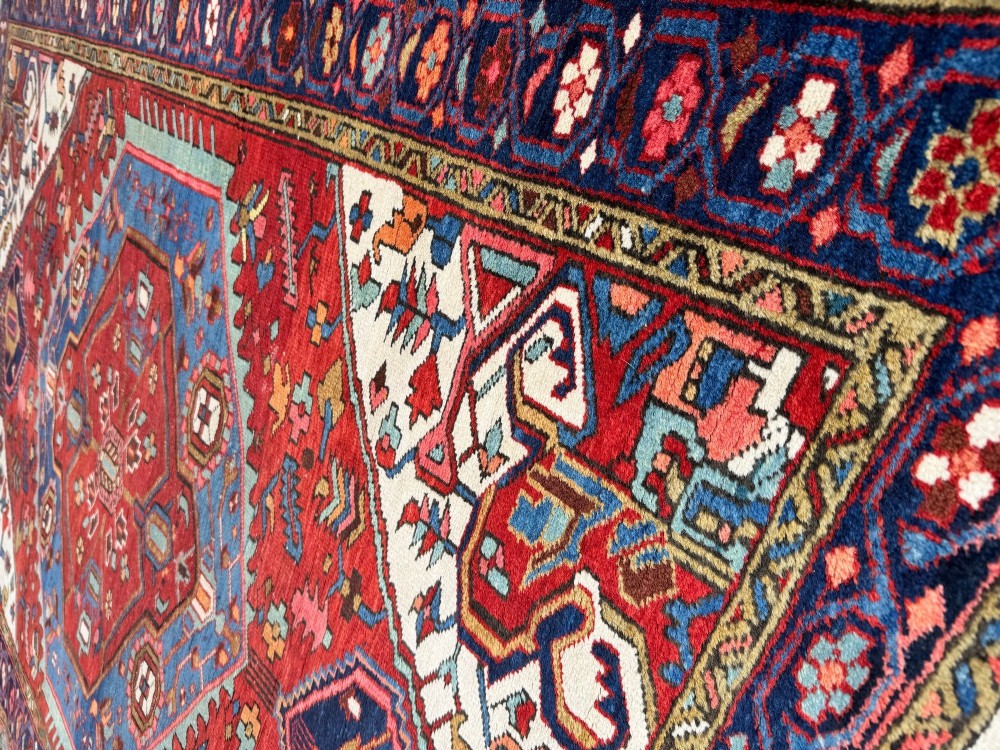 An antique Heriz wool rug featuring a large geometric central medallion in blue and red surrounded by cream spandrels and a navy border. View IX