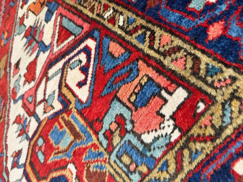 An antique Heriz wool rug featuring a large geometric central medallion in blue and red surrounded by cream spandrels and a navy border. View X