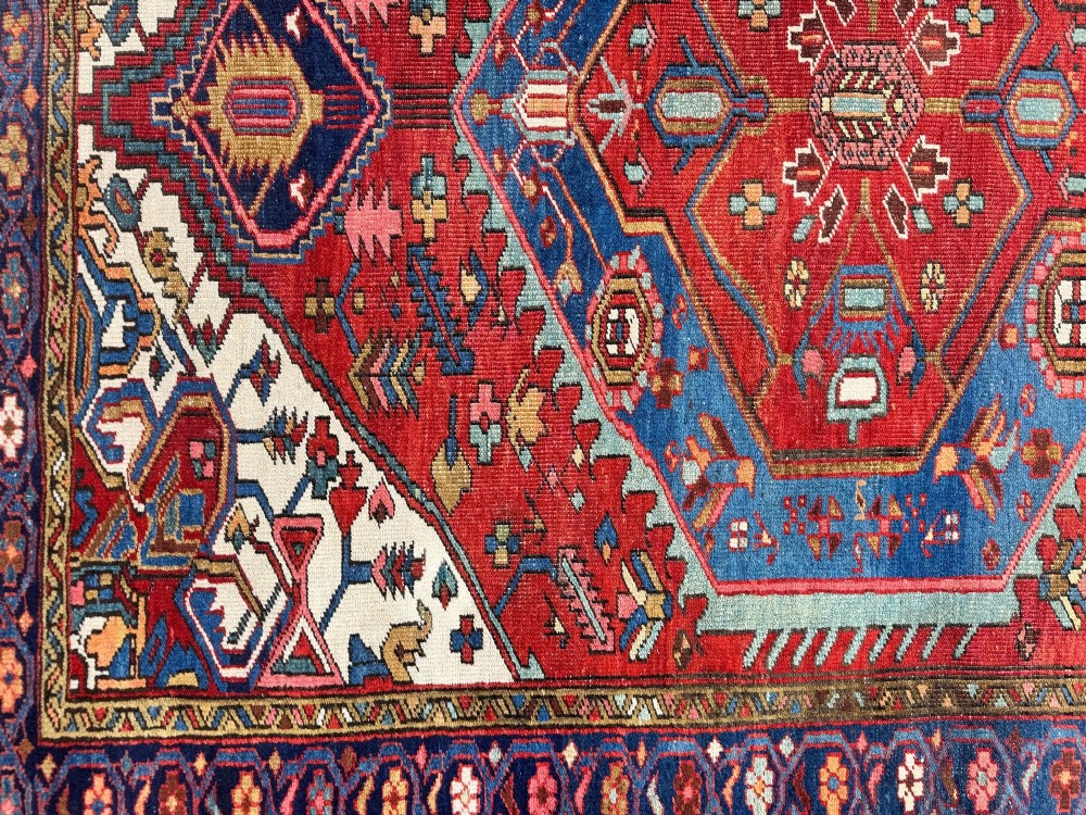 An antique Heriz wool rug featuring a large geometric central medallion in blue and red surrounded by cream spandrels and a navy border. View XII