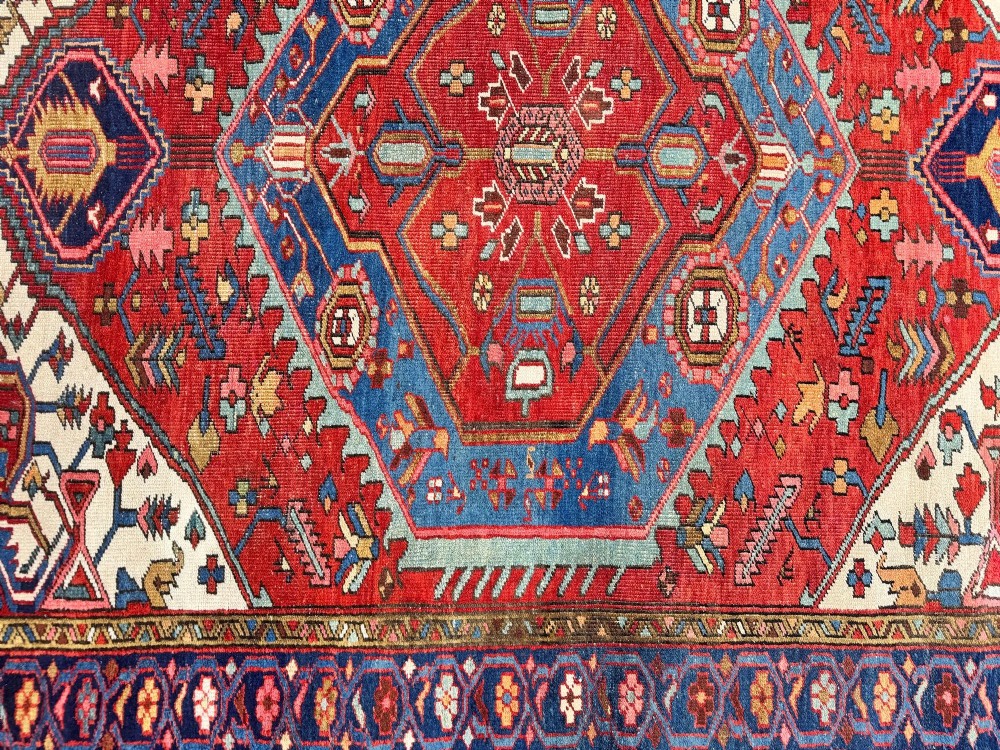 An antique Heriz wool rug featuring a large geometric central medallion in blue and red surrounded by cream spandrels and a navy border. View XIII