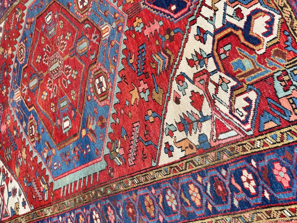 An antique Heriz wool rug featuring a large geometric central medallion in blue and red surrounded by cream spandrels and a navy border. View XIV