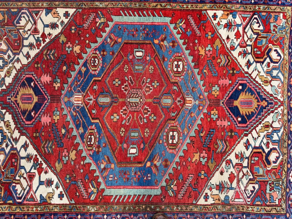 An antique Heriz wool rug featuring a large geometric central medallion in blue and red surrounded by cream spandrels and a navy border. View XV