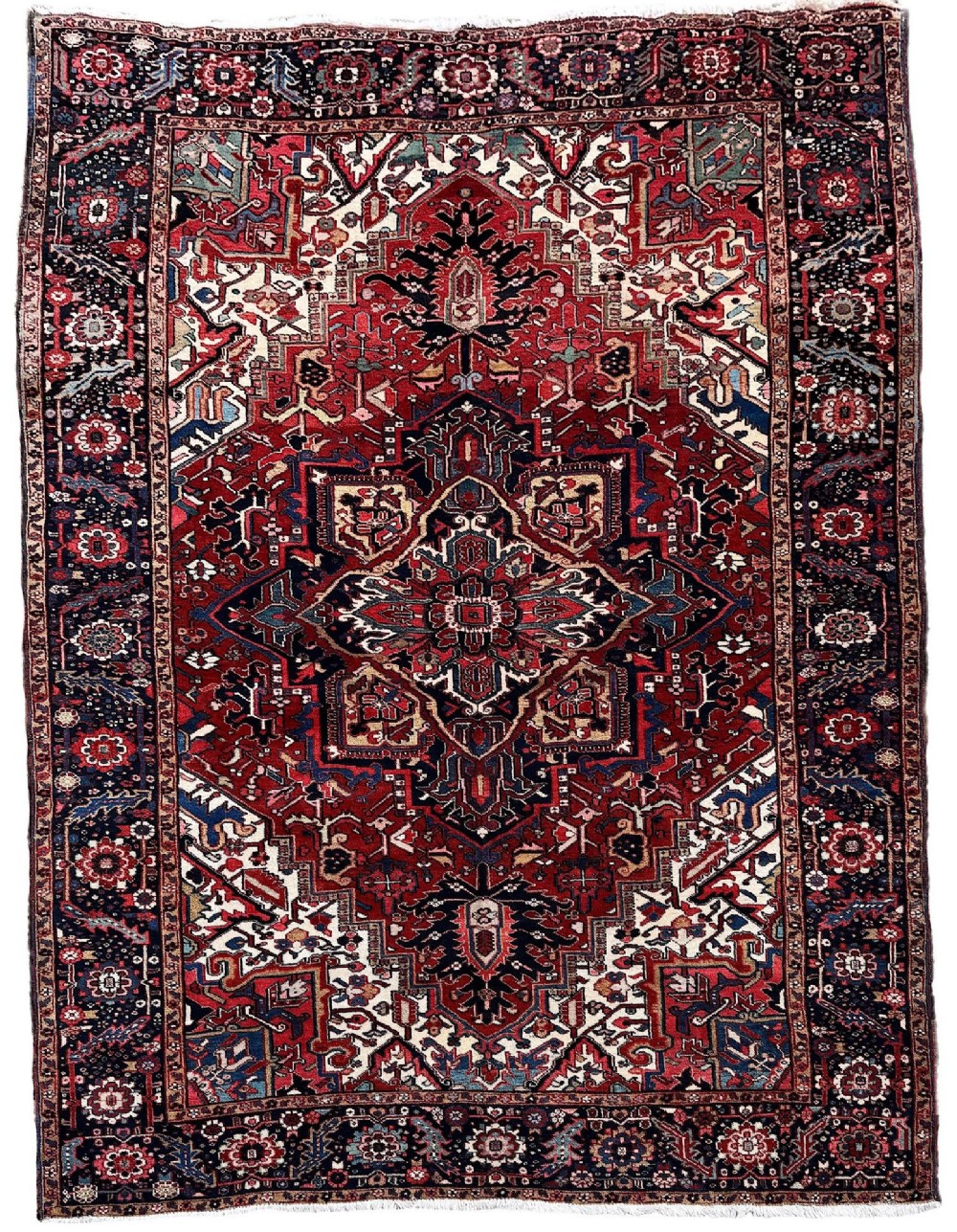 An antique hand-knotted Persian Heriz carpet featuring a prominent geometric central medallion on a rust red field with cream corner spandrels and a navy blue border.
