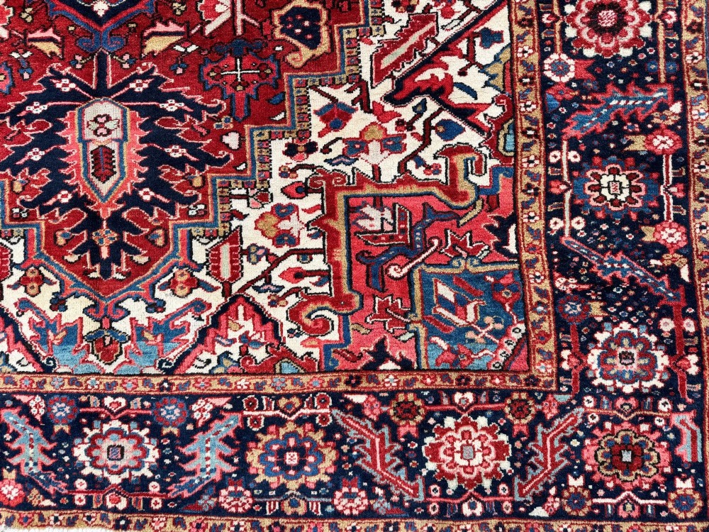An antique hand-knotted Persian Heriz carpet featuring a prominent geometric central medallion on a rust red field with cream corner spandrels and a navy blue border. View VI