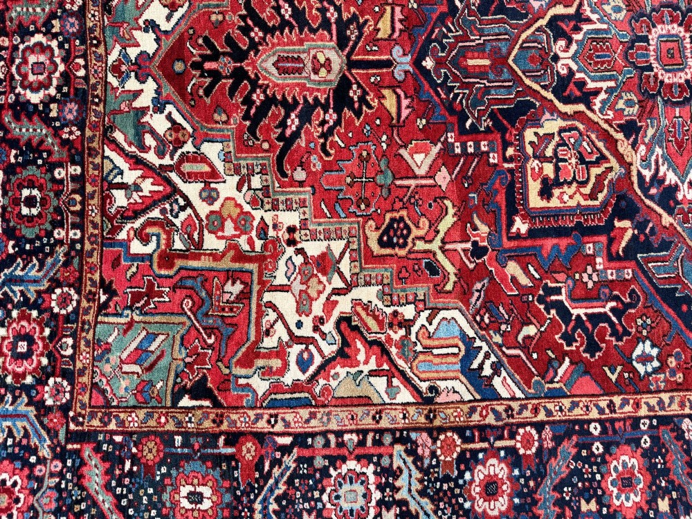 An antique hand-knotted Persian Heriz carpet featuring a prominent geometric central medallion on a rust red field with cream corner spandrels and a navy blue border. View VII