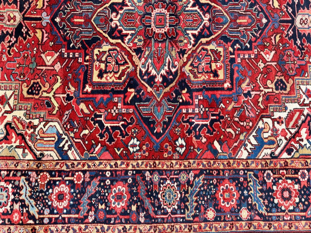 An antique hand-knotted Persian Heriz carpet featuring a prominent geometric central medallion on a rust red field with cream corner spandrels and a navy blue border. View VIII