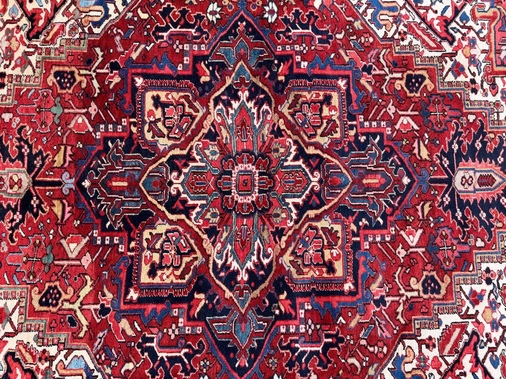 An antique hand-knotted Persian Heriz carpet featuring a prominent geometric central medallion on a rust red field with cream corner spandrels and a navy blue border. View IX