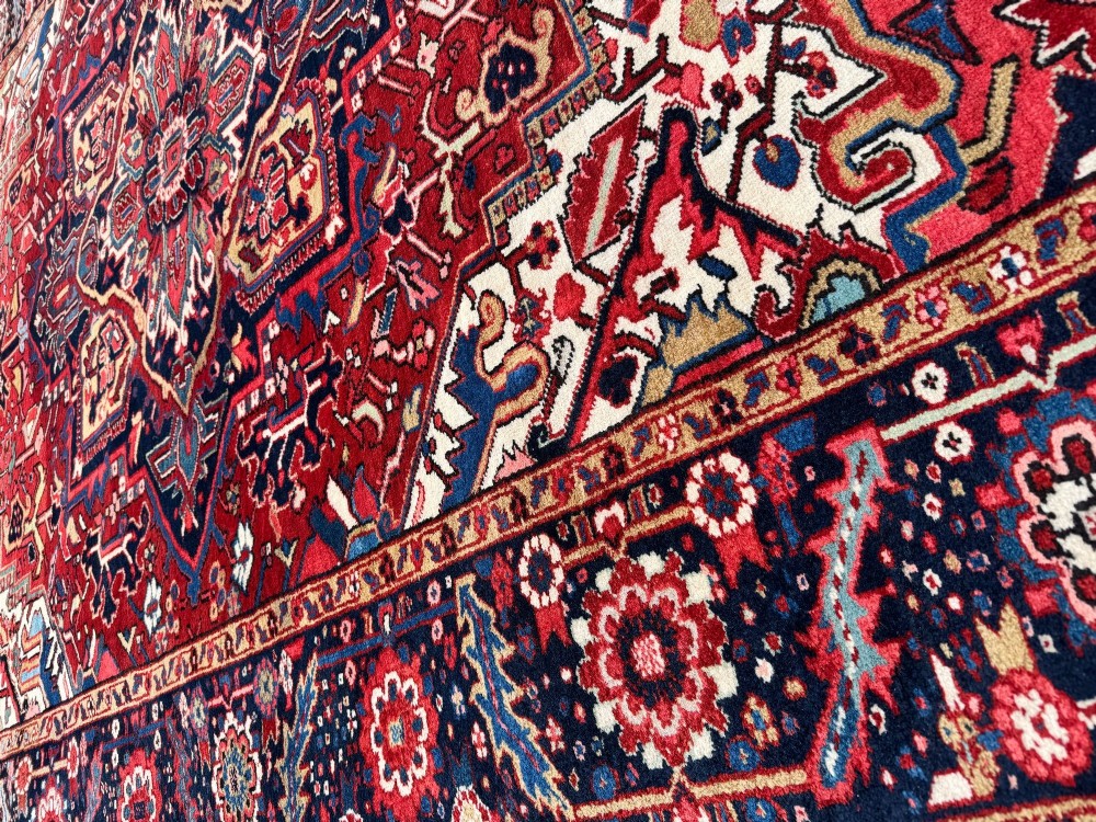 An antique hand-knotted Persian Heriz carpet featuring a prominent geometric central medallion on a rust red field with cream corner spandrels and a navy blue border. View X