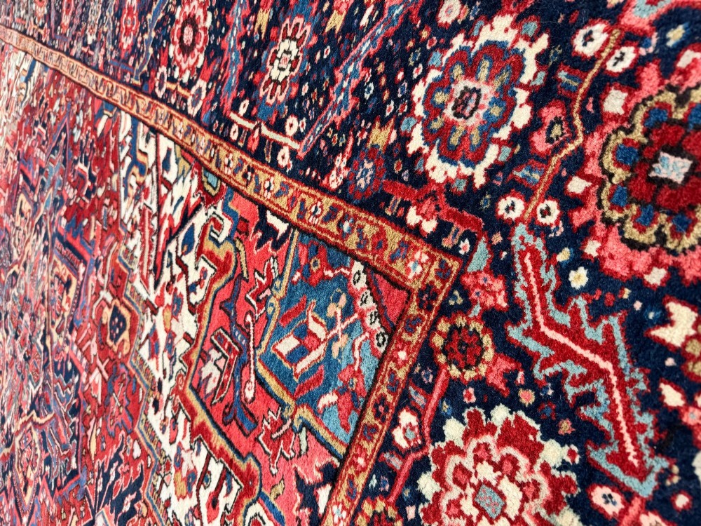 An antique hand-knotted Persian Heriz carpet featuring a prominent geometric central medallion on a rust red field with cream corner spandrels and a navy blue border. View XV