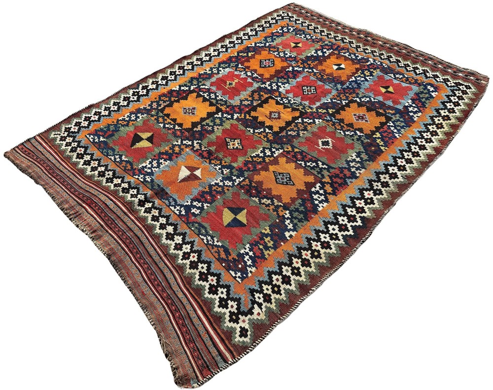 An antique handwoven Qashqai wool kilim rug featuring geometric stepped diamond motifs in terracotta red, ochre orange, indigo blue, and ivory. View III