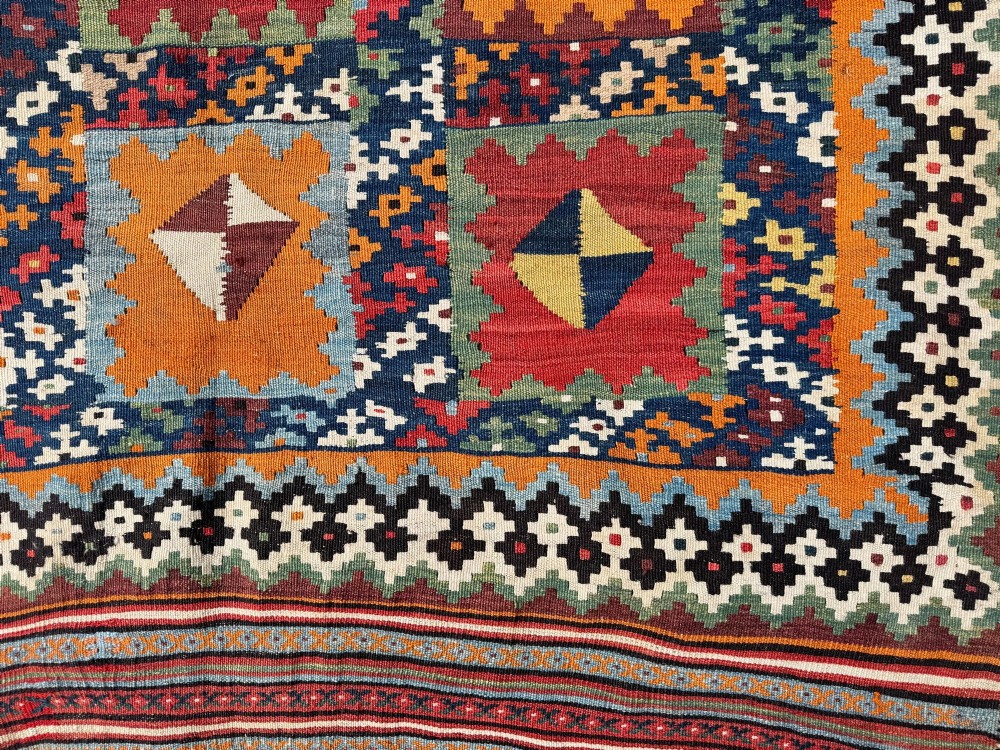An antique handwoven Qashqai wool kilim rug featuring geometric stepped diamond motifs in terracotta red, ochre orange, indigo blue, and ivory. View VII