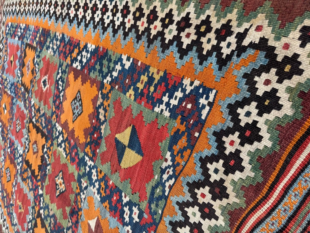 An antique handwoven Qashqai wool kilim rug featuring geometric stepped diamond motifs in terracotta red, ochre orange, indigo blue, and ivory. View IX