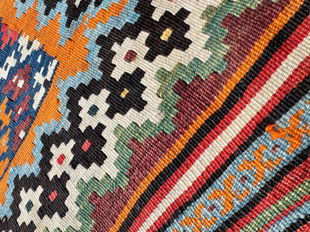 An antique handwoven Qashqai wool kilim rug featuring geometric stepped diamond motifs in terracotta red, ochre orange, indigo blue, and ivory. View X