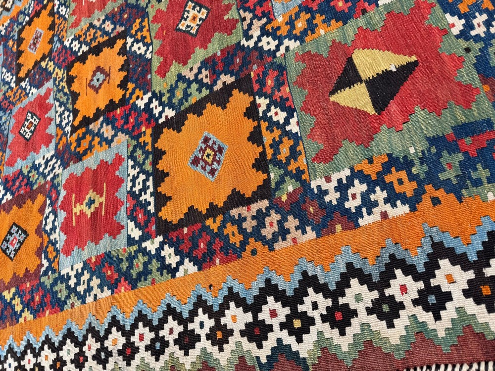 An antique handwoven Qashqai wool kilim rug featuring geometric stepped diamond motifs in terracotta red, ochre orange, indigo blue, and ivory. View XV