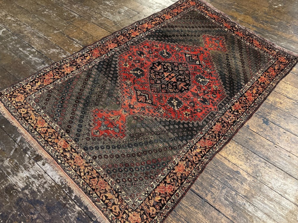 An antique hand-knotted Bakhtiar wool rug featuring a central terracotta stepped medallion on a dark indigo field filled with intricate floral motifs. View V