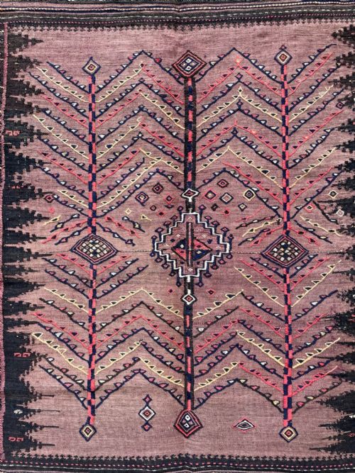 fig 1. A square antique handwoven Ru Korsi textile featuring a dusty purple central field with chevron tree motifs bordered by dark geometric band patterns.