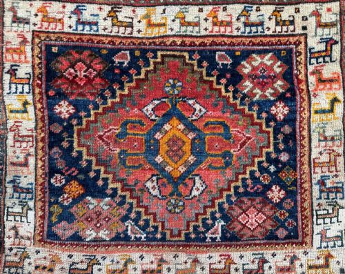 fig 1. A pair of square hand-woven wool Qashqai saddlebag faces featuring central geometric diamond medallions surrounded by borders of stylised animal figures in terracotta red, navy blue, and ivory.