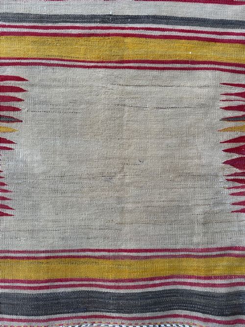 fig 2. A square antique flatwoven Persian Sofreh textile featuring red, yellow, and grey horizontal stripes bordering an unpatterned central cream field with serrated side accents.