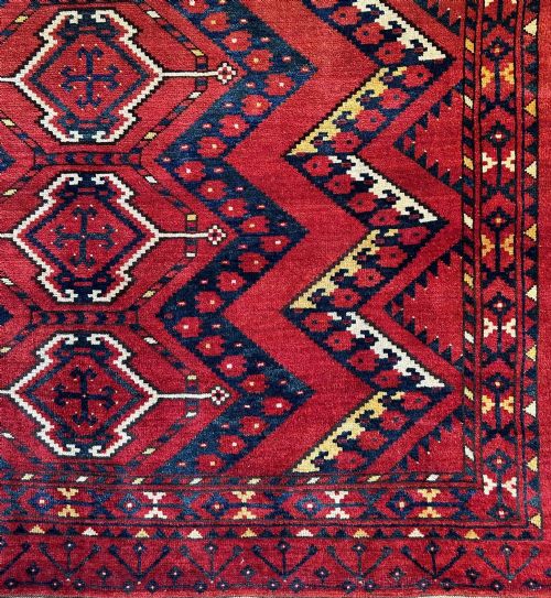 fig 2. A rectangular hand-knotted wool Turkmen storage bagface featuring central diamond motifs woven in crimson red, dark navy blue, yellow, and cream with fringed edges.