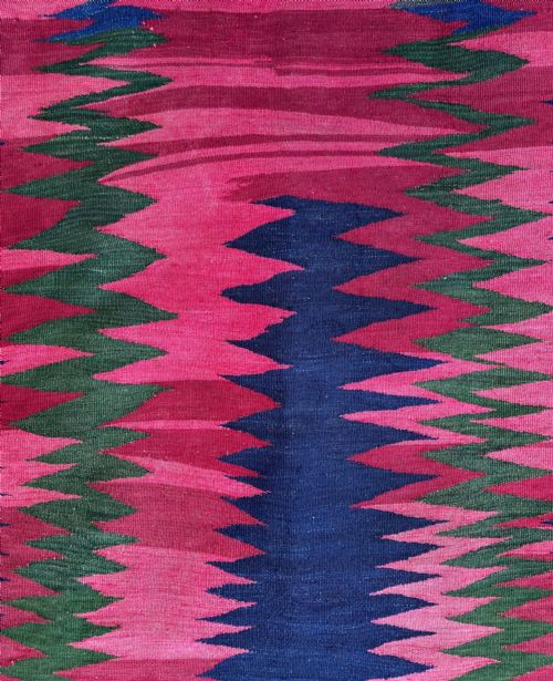 fig 1. A square handwoven flatweave textile featuring bold zigzag patterns in magenta, green, and dark blue wool with decorative border motifs.