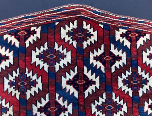 fig 1. A pentagonal handwoven Turkmen Asmalyk wool textile featuring geometric diamond lattice patterns in red, dark blue, and white.