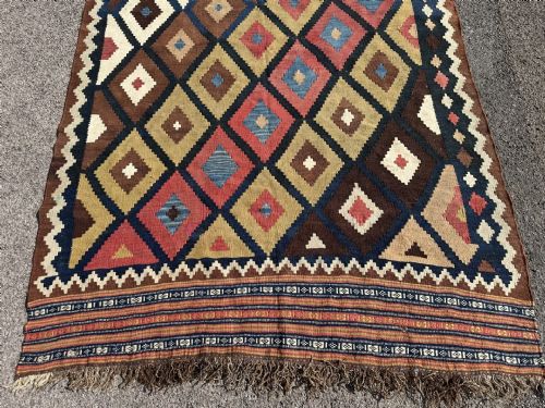 fig 1. An antique handwoven Persian Qashqai wool kilim rug featuring repeating geometric diamond motifs in terracotta, dark brown, blue, yellow, and cream hues.