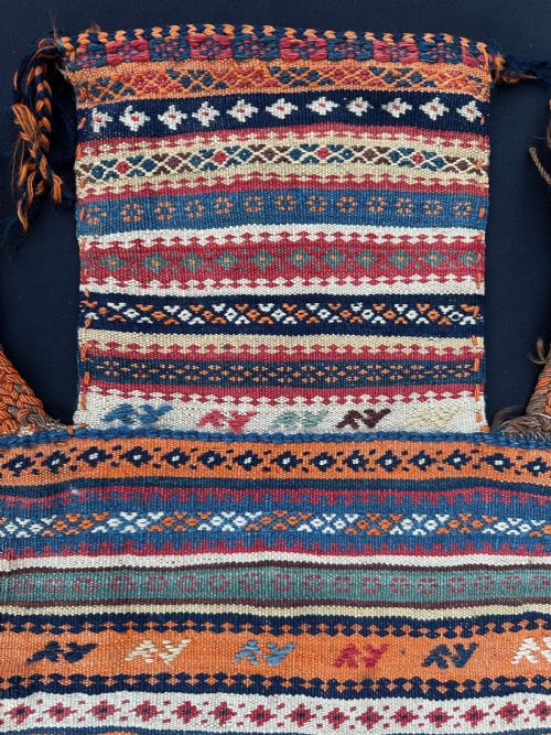 fig 1. A handwoven antique Qashqai salt bag featuring horizontal bands of geometric patterns in orange, blue, red, and white wool with braided side loops.
