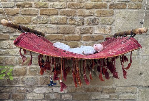 fig 1. A handwoven red wool tribal textile featuring geometric motifs, hanging tassels, leather loops, and top and bottom wooden support rods.