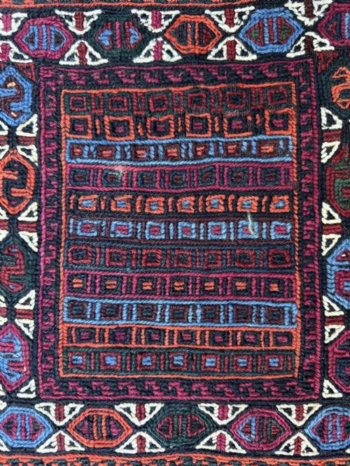 fig 1. An antique Persian tribal bag displaying geometric woven patterns in red, blue, and orange with a heavy fringe embellished with cowrie shells and tassels.